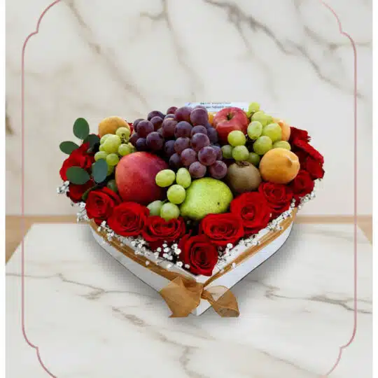 Arreglo floral ARMANI con frutas frescas variadas y rosas rojas dispuestas en una caja blanca en forma de corazón, ideal para