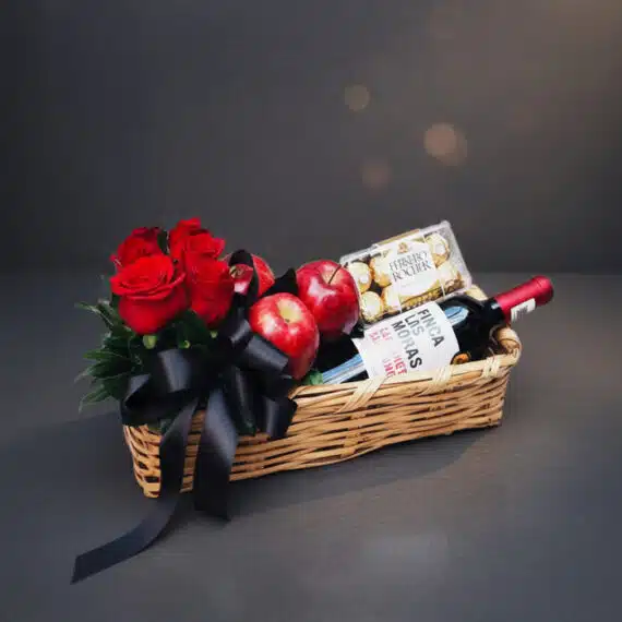 Arreglo ANGELO: Cesta Elegante con Rosas Rojas, Vino y Chocolates Arreglo ANGELO: Elegante cesta de mimbre con rosas rojas frescas, manzanas rojas, botella de vino tinto Finca Las Moras y caj