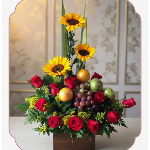 Arreglo floral Batista con rosas rojas, girasoles vibrantes, uvas, mandarinas y manzanas verdes en una base de madera, ideal