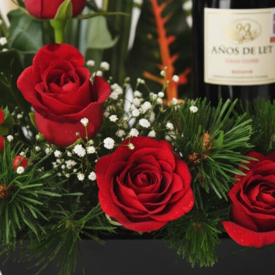 Primer plano extremo de arreglo floral CINZIA con 12 rosas rojas, gotas de rocío, follaje verde y botella de vino tinto.