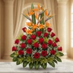 Arreglo floral exótico Tucana con rosas rojas, lirios naranjas y aves del paraíso, sobre mármol en un lobby elegante.