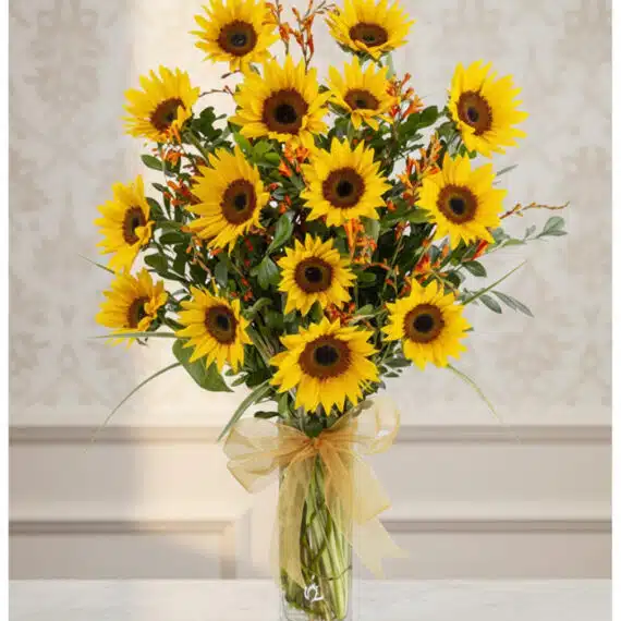 Arreglo Floral de Girasoles LENU: Radiante Belleza para Tu Hogar Arreglo floral de girasoles LENU en un jarrón de cristal con lazo dorado, sobre una mesa de mármol y fondo elegante.