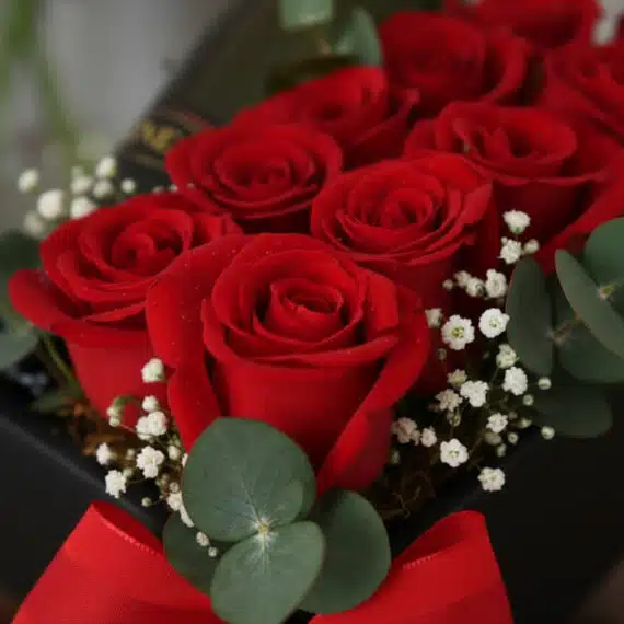 Primer plano extremo de Arreglo Floral NATALE con rosas rojas vibrantes, gotas de rocío sutiles, eucalipto y gypsophila en ca