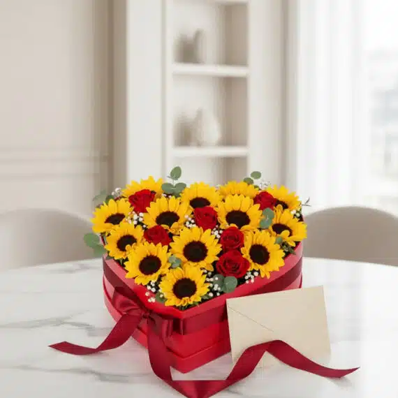 Arreglo floral RINA en forma de corazón con girasoles vibrantes y rosas rojas, presentado en una caja roja con cinta de satén