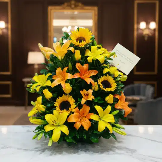 Arreglo floral tropical vibrante con girasoles, lirios amarillos y naranjas, y follaje verde, sobre una superficie de mármol