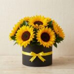 Arreglo floral de girasoles MARISA en caja negra con lazo amarillo, ideal para ecommerce de floristería, con fondo elegante e