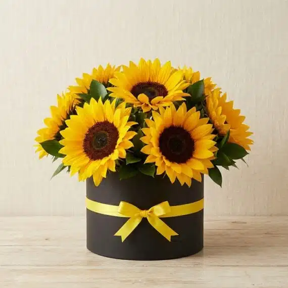 Arreglo de Girasoles MARISA: Elegancia y Alegría para Regalar Arreglo floral de girasoles MARISA en caja negra con lazo amarillo, ideal para ecommerce de floristería, con fondo elegante e