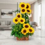 Arreglo floral con girasoles vibrantes y follaje verde en una base de madera, sobre una superficie de mármol pulido en un ent