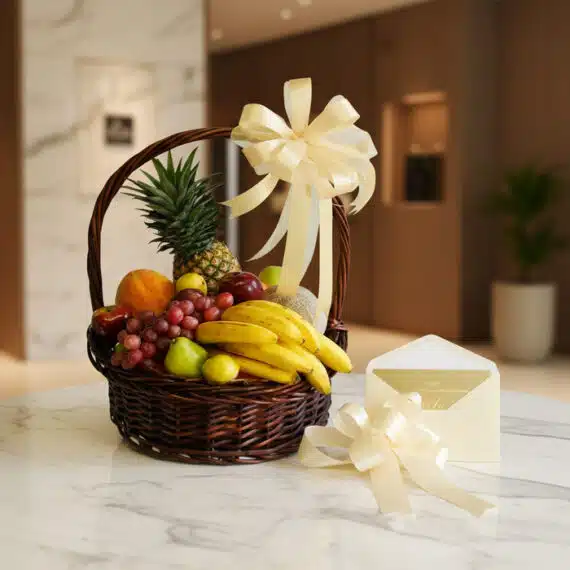 Canasta de Frutas Sirio con piña, uvas, plátanos, manzanas y peras, decorada con un lazo crema y una tarjeta de regalo elegan