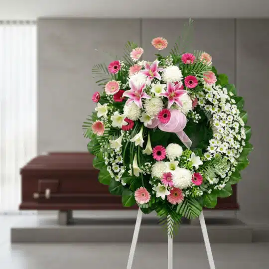 Corona fúnebre solemne 'Homenaje a Mathias' con flores blancas, rosas y follaje verde, en una sala de velación moderna con at
