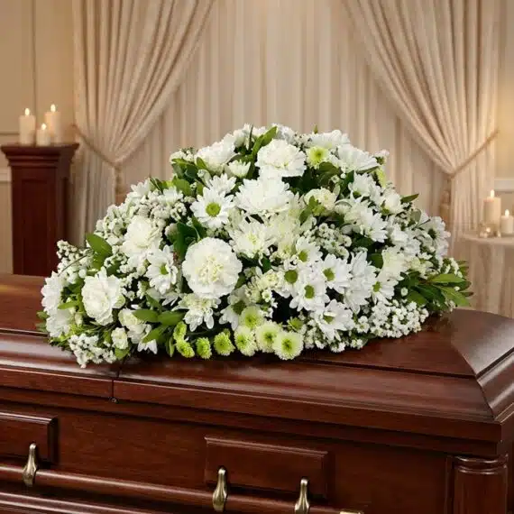 Cubre Caja Fúnebre Epifania: Homenaje Floral de Distinción y Serenidad Cubre caja fúnebre Epifania con flores blancas sobre un ataúd de madera oscura, en un entorno elegante y sereno con iluminaci