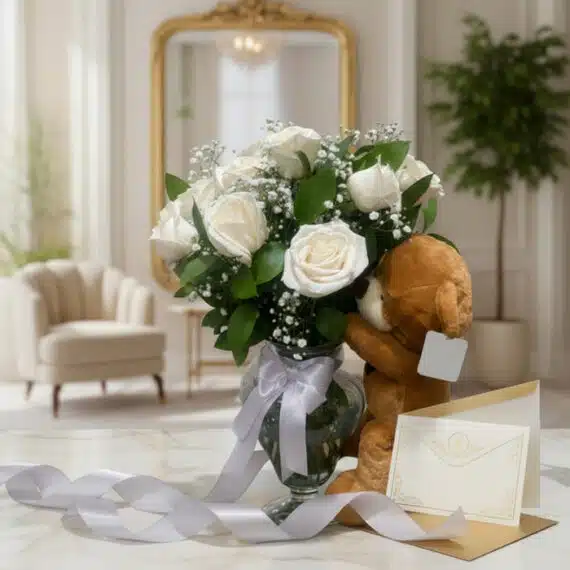 Jarrón Llévame Contigo con un hermoso arreglo de rosas blancas frescas y follaje, acompañado de un osito de peluche abrazando