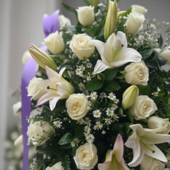 Primer plano de un pedestal fúnebre 'Salvación' con rosas blancas, lirios y follaje verde, destacando texturas y rocío sutil.